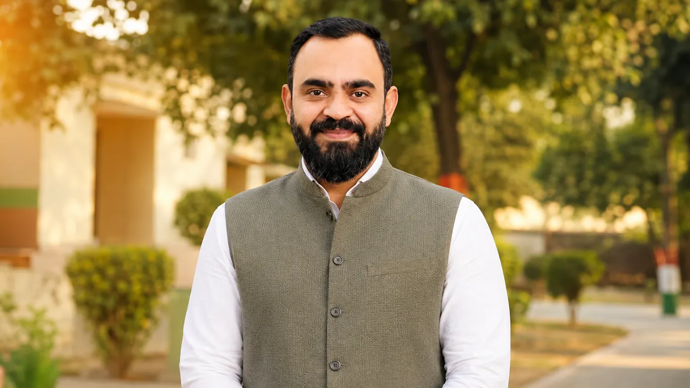 Agam Chaudhary, wearing a white kurta and an olive Nehru jacket, photographed outdoors on a tree-lined path